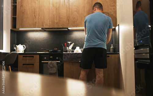 Man washes dishes in the kitchen sink in the evening. photo