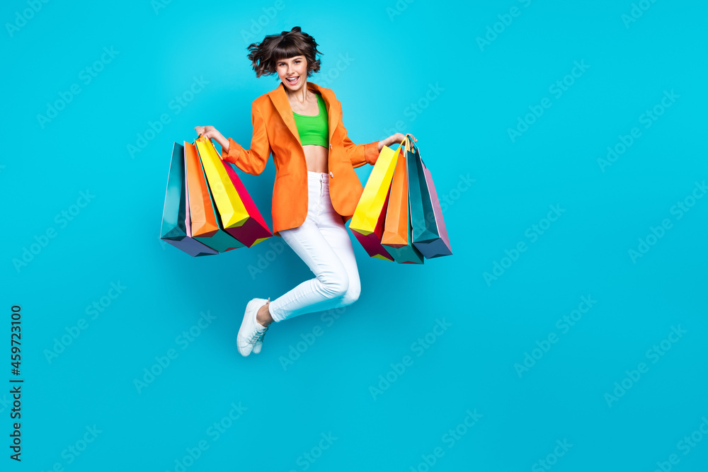 Full length photo of young cheerful woman jump up air hold shopping bags enjoy isolated on blue color background Full length photo of young cheerful woman jump up air hold shopping bags enjoy isolated on blue color background