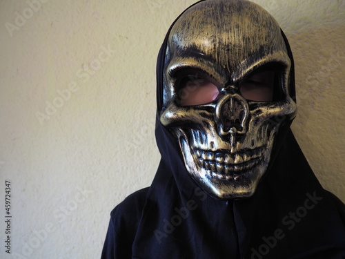 Boy guiser. A child in a mask of a scary skull with a black hood. Black clothes. Halloween, All Hallows Even or All Saints Even. Carnival costume. Portrait and copy space photo