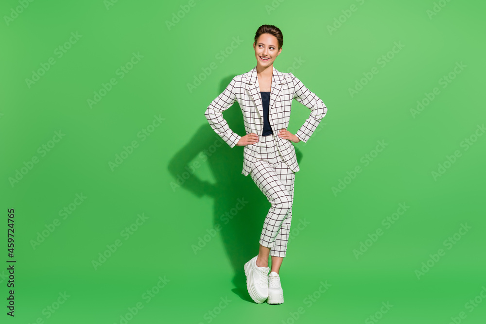 Photo of cute charming young woman dressed checkered clothes arms waist looking empty space smiling isolated green color background Photo of cute charming young woman dressed checkered clothes arms waist looking empty space smiling isolated green color background