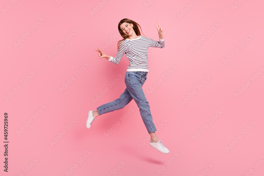 Full length body size view of attractive cheerful girl jumping showing v-sign going isolated over pink pastel color background Full length body size view of attractive cheerful girl jumping showing v-sign going isolated over pink pastel color background