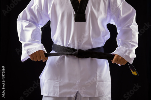 Close up Taekwondo martial arts fighter in white uniform two hands holding black belt on dark background photo