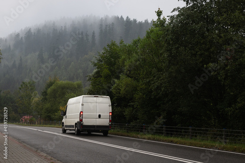 White truck is on mountain highway winding through forested landscape in autumn colors - business, commercial, cargo transportation concept, clear and blank space on the side view