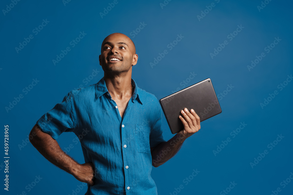 Black bold man wearing shirt smiling while posing with tablet computer Black bold man wearing shirt smiling while posing with tablet computer