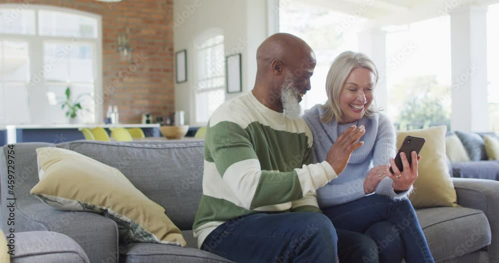 Happy senior diverse couple in living room sitting on sofa, using smartphone, making video call Happy senior diverse couple in living room sitting on sofa, using smartphone, making video call