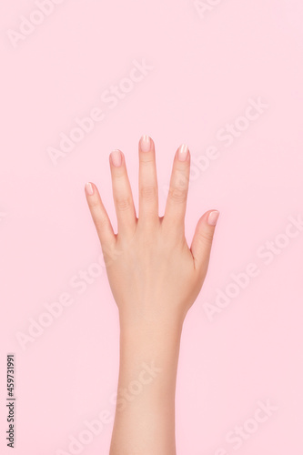 Female hand with beautiful manicure - pink nude nails on pink background. Nail care concept