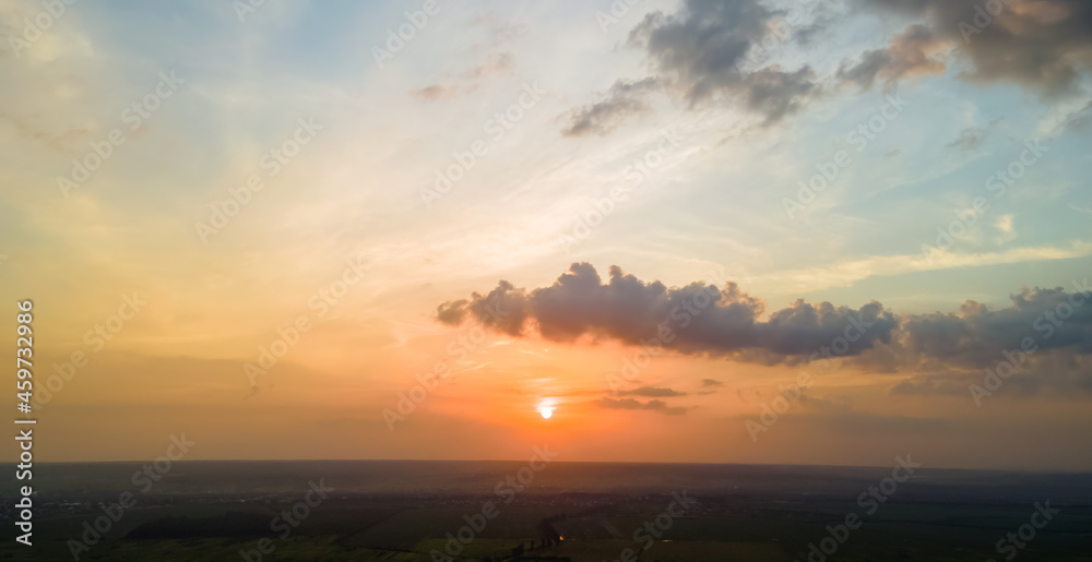 Obraz premium Bright colorful sunset sky with setting sun and vibrant clouds over dark landscape.