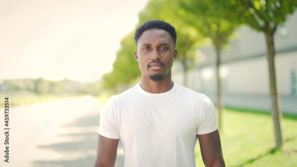 Portrait confident African American athlete standing urban background city park or stadium looking at camera Happy, cheerful male fitness trainer coach smiling. man in white t-shirt outdoors, outside Portrait confident African American athlete standing urban background city park or stadium looking at camera Happy, cheerful male fitness trainer coach smiling. man in white t-shirt outdoors, outside