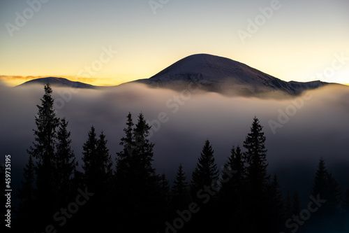 Beautiful mountain landscape with hazy peaks and foggy wooded valley at sunset. © bilanol