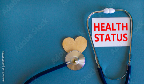 Health status symbol. White card with words Health status, beautiful blue background, wooden heart and stethoscope. Medical, health status concept.