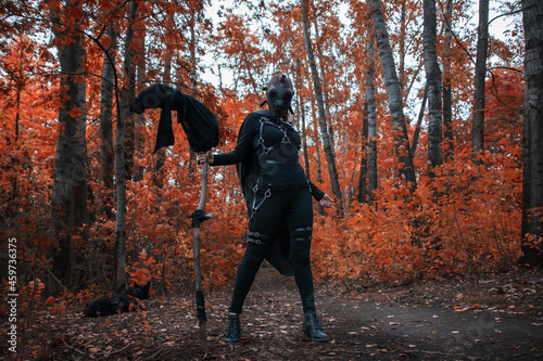 a girl in a bdsm costume and a black mask in a red forest.an idea for halloween