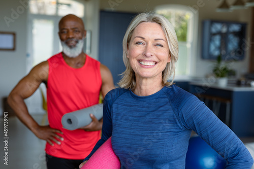 Portrait of happy senior diverse couple in exercise clothes practicing yoga, looking at camera