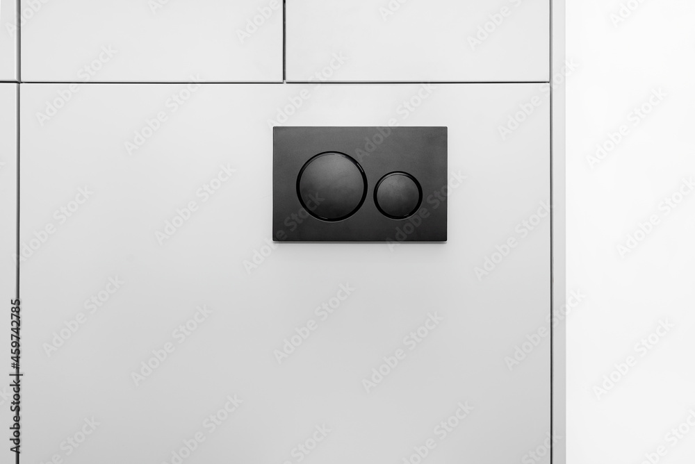 Black matt toilet flush with two round buttons placed in the wall of a restroom lined with a wooden panel. Black matt toilet flush with two round buttons placed in the wall of a restroom lined with a wooden panel.