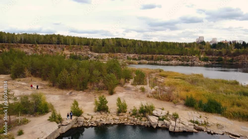 Aerial Dolly Pan Over A Stone Quarry Flooded With Water. People Walk Along The Shore With Growing Trees And Reeds Aerial Dolly Pan Over A Stone Quarry Flooded With Water. People Walk Along The Shore With Growing Trees And Reeds