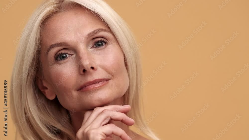 A close-up view of the middle aged cheerful woman looking at the camera in the beige studio A close-up view of the middle aged cheerful woman looking at the camera in the beige studio