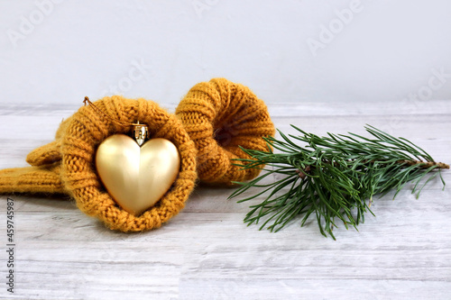 The concept of the arrival of New Year's holidays. Christmas tree toy in the shape of a heart in a warm yellow mitten, a pine branch next to it, gray background, a place for text