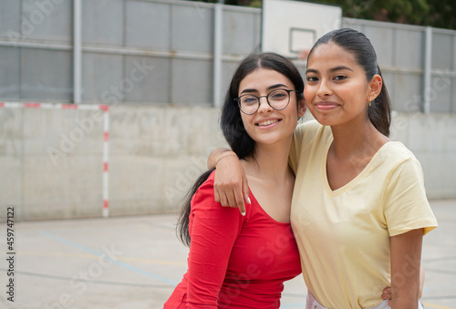 Two Student teenager girls from different races outside high school. Portrait of multiracial female friends in a playground.  photo