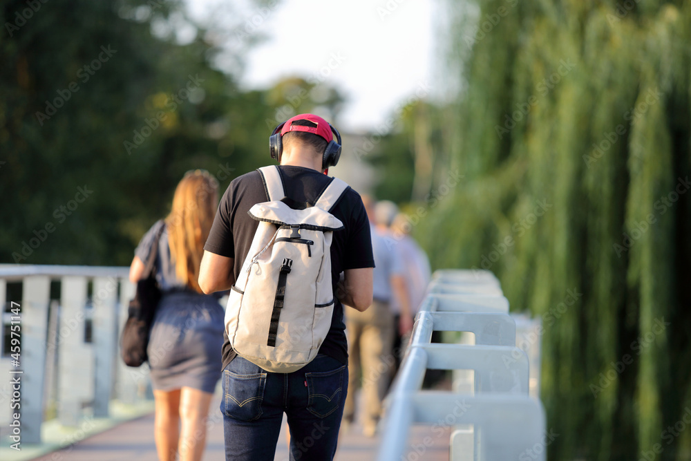 Młody mężczyzna z plecakiem i słuchawkami na uszach, idzie po moście we Wrocławiu. - obrazy, fototapety, plakaty 