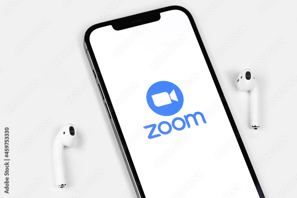 Zoom mobile logo app on screen smartphone iPhone with AirPods on white background. Zoom Video