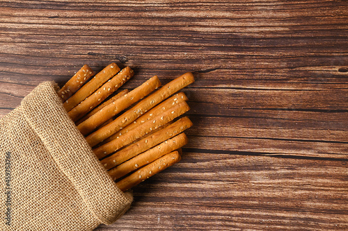 Grissini are in sackcloth. Crispy white sticks on a brown background. With sesame seeds. The appetizer is delicious.