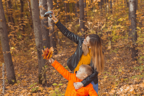 Son and mother are taking selfie on camera in autumn park. Single parent, leisure and fall season concept.