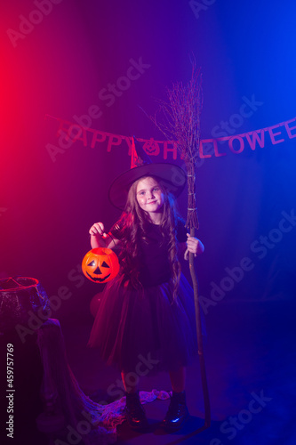 Little girl holds broom on Halloween holiday. Kid girl wear witch costume. Fantasy, fairy tale and masquerade concept. © satura_