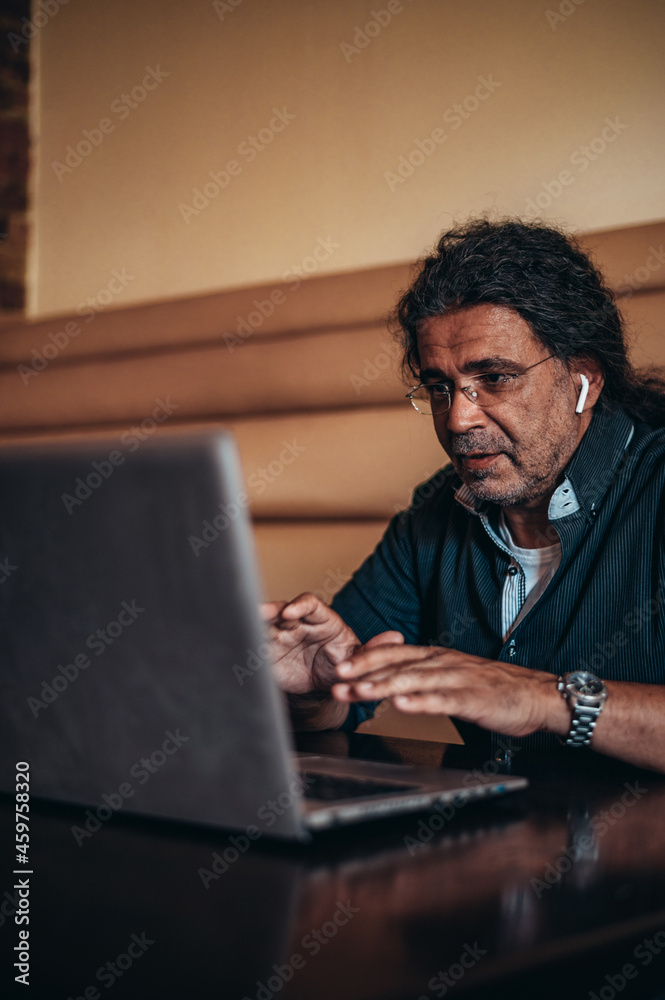 Senior hispanic cuban man using laptop and airpods in a cafe Senior hispanic cuban man using laptop and airpods in a cafe