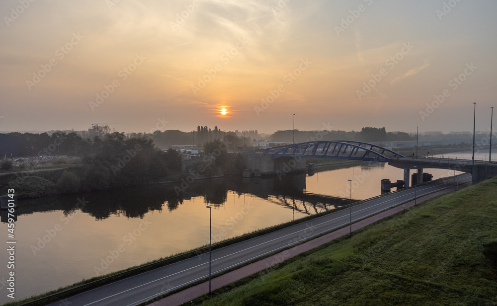 Aerial drone shot of flying over calm water on a canal at sunrise and over a bridge in Boom, Antwerp Belgium