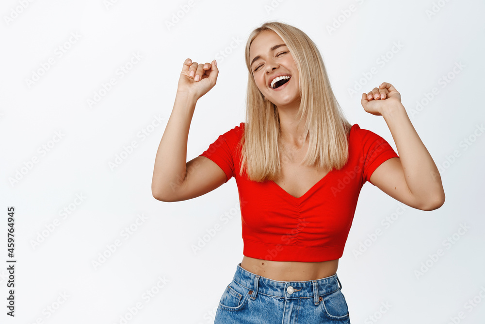 Carefree blond girl dancing, laughing and having fun, standing in cropped top against white background Carefree blond girl dancing, laughing and having fun, standing in cropped top against white background