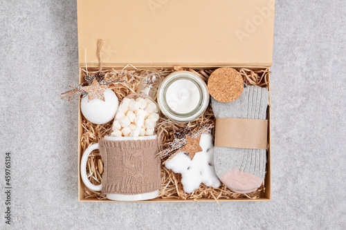 Preparing care package, seasonal gift box with mug, candle, woolen socks and christmas ornament. Personalized eco friendly basket for winter holidays. Top view, flat lay photo