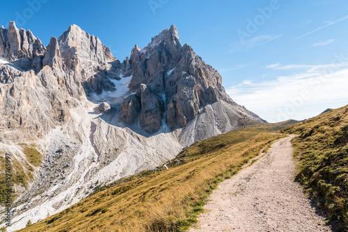 Empty high altitute gravel path running at the foot of a towering rocky peak in the European Alps on a sunny autumn day