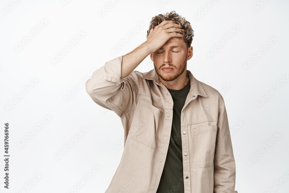 Frustrated blond man facing failure, facepalm and look distressed, being in trouble, standing upset against white background