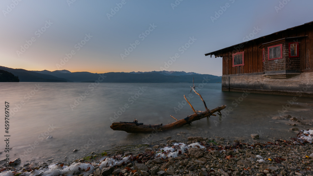 Idyllic calm soothing morning scenery at mountain lake Walchensee in Bavaria, Germany at dawn with boat house and dead tree branch