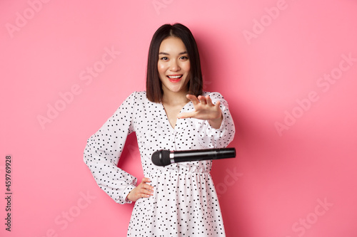 Happy asian woman drop the microphone, smiling and looking confident at camera, standing over pink background photo