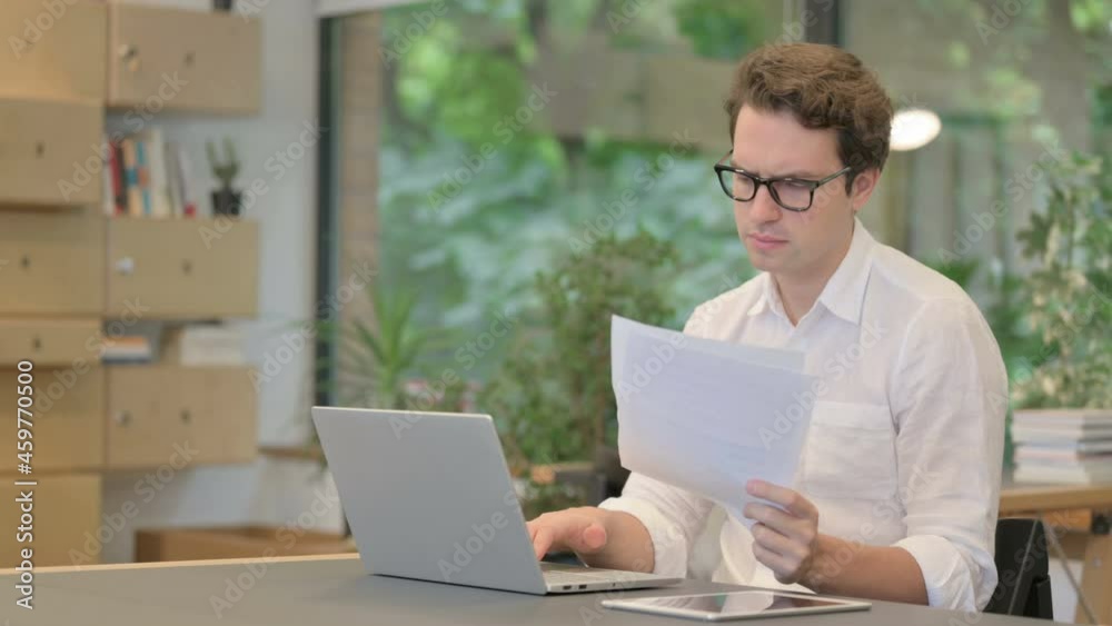 Man with Laptop Reading Documents in Modern Office 
