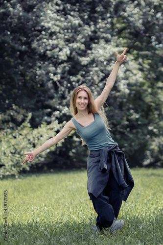 Smiling girl stands in a pose of pointing fingers up and down on a green meadow in the park