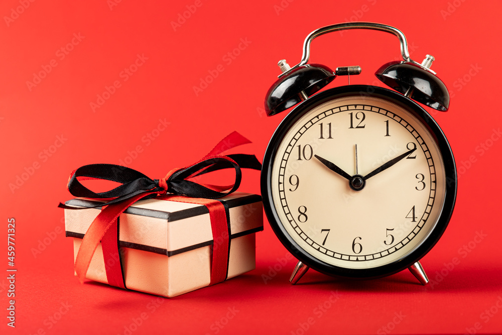gift box and alarm clock on a red background, time for shopping.