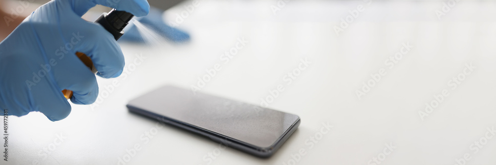 Person in gloves treats smartphone with disinfectant closeup Person in gloves treats smartphone with disinfectant closeup