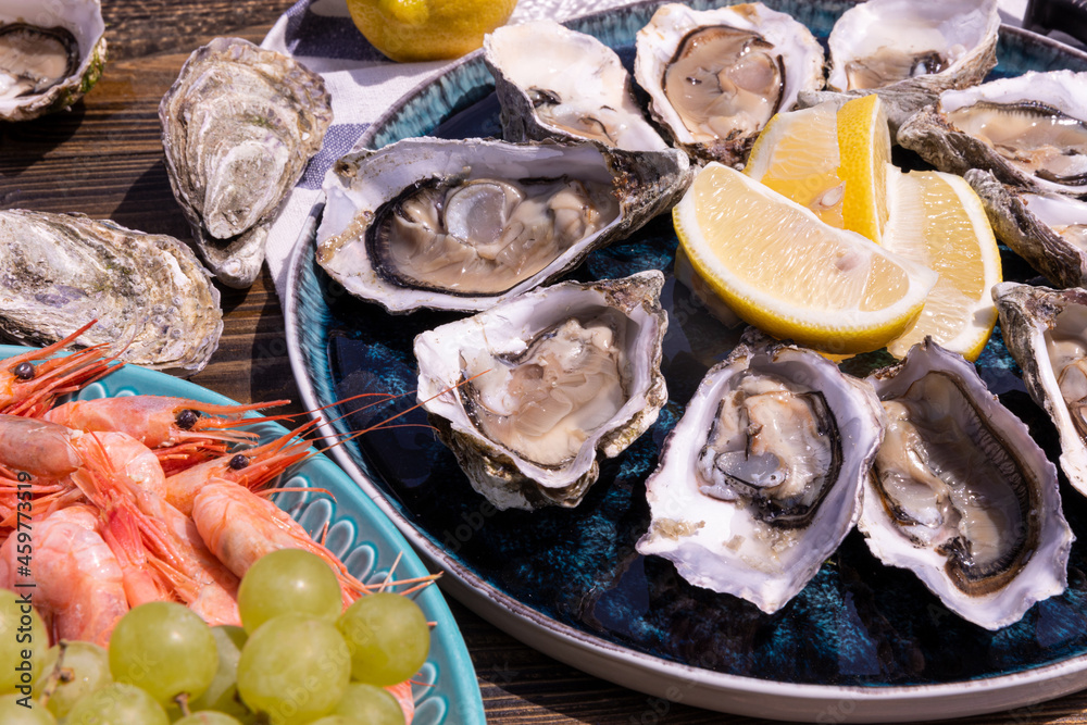resh oysters with lemon slices on a platter, shrimp with grapes on a platter, on a wooden background.