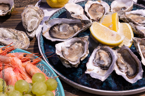 resh oysters with lemon slices on a platter, shrimp with grapes on a platter, on a wooden background.
