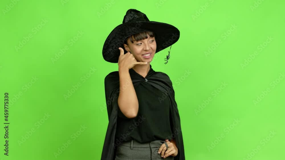 Young woman wearing witch hat for halloween parties making phone gesture and speaking with someone. Call me back sign over isolated background Young woman wearing witch hat for halloween parties making phone gesture and speaking with someone. Call me back sign over isolated background