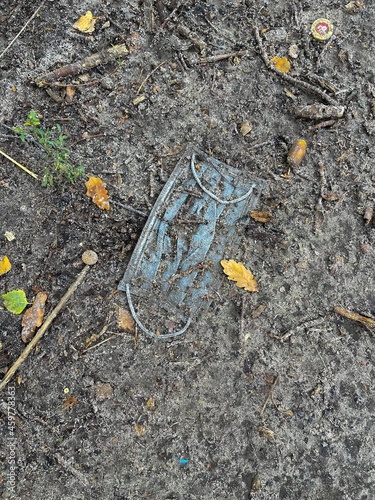 Vertical top view shot of a medical face mask laying in the dirt on the ground