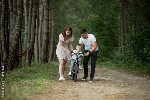 Young family on a picnic in the woods, husband, wife and young child son, teach son to ride a bicycle