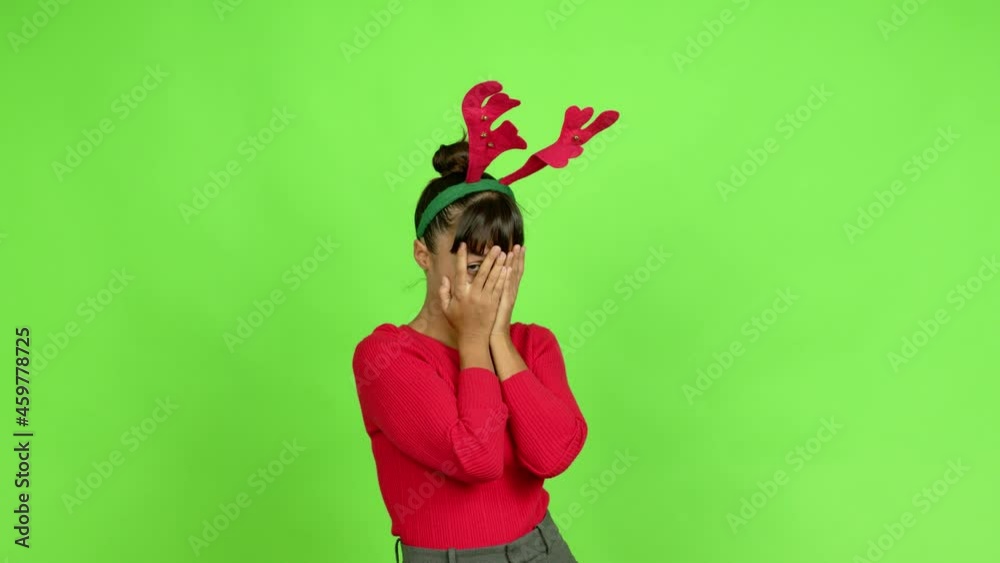 Young woman wearing christmas hat covering eyes by hands and looking through the fingers over isolated background. Green screen chroma key Young woman wearing christmas hat covering eyes by hands and looking through the fingers over isolated background. Green screen chroma key