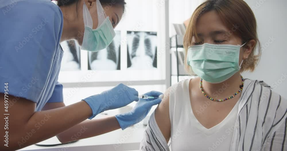 Young Asia lady nurse giving Covid-19 or flu antivirus vaccine shot to teenage girl patient wear face mask protection from virus disease at health clinic or hospital office. Close up or Closeup shot. Young Asia lady nurse giving Covid-19 or flu antivirus vaccine shot to teenage girl patient wear face mask protection from virus disease at health clinic or hospital office. Close up or Closeup shot.