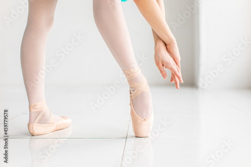 Ballerina's feet in ballet pointe shoes and hands. She's dancing in white room