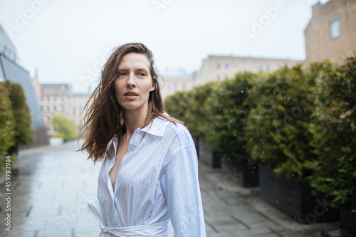 Happy woman in the rain. Portrait of a girl. Daily energy in city life. Portrait of female with wet hair and wet dress. Green life at urban environment. close up portrait. Summer joy © Girts