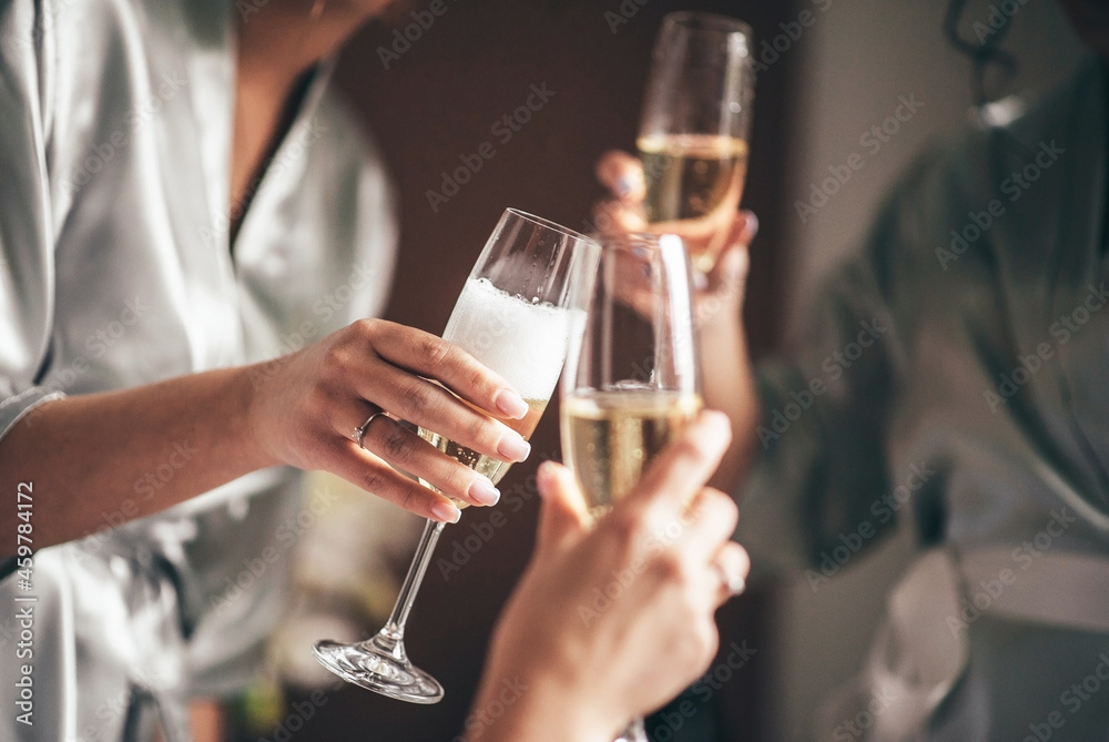 bride with bridesmaids indoors with a ring on her hand holding glasses of champagne in her hands, close-up front view
