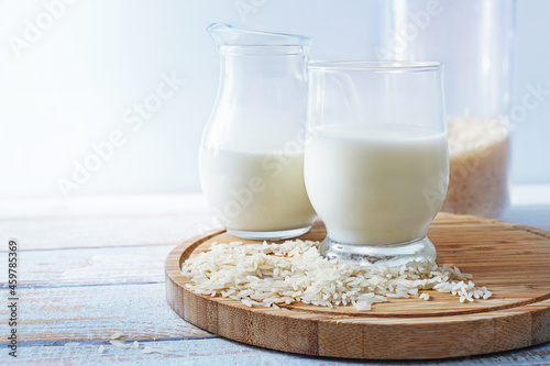 Vegan rice milk, healthy alternative without animal dairy products in a drinking glass and a jug on a wooden kitchen board against a light background, copy space, selected focus photo