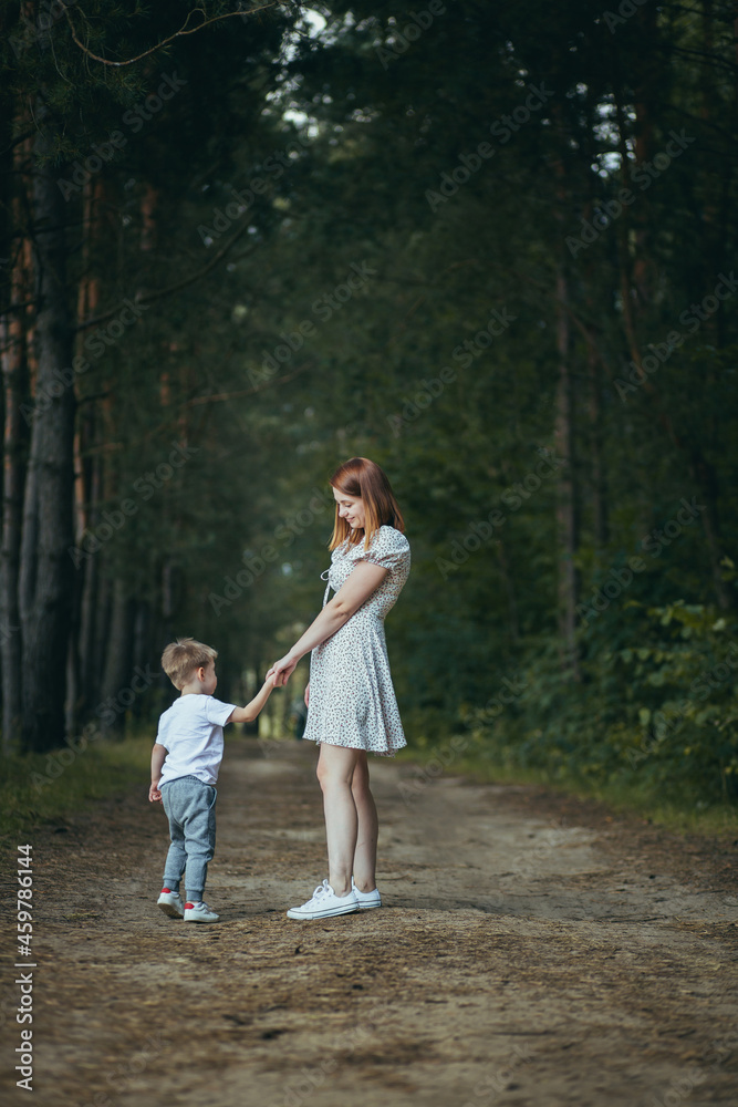 Fototapeta premium young woman mom walks with little baby son in the woods hand teaches to walk
